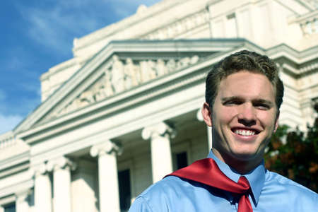 happy young man is leaving the courthouse with a blue shirt and red tieの写真素材