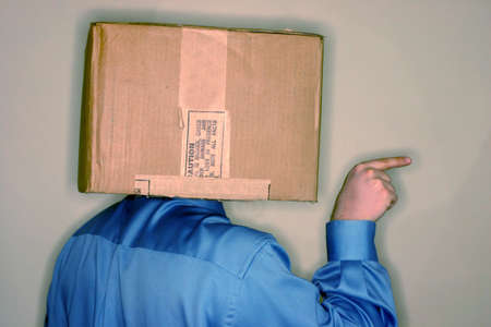 Business man wearing blue shirt has carboard box over his head as he is pointing out towards the sideの写真素材