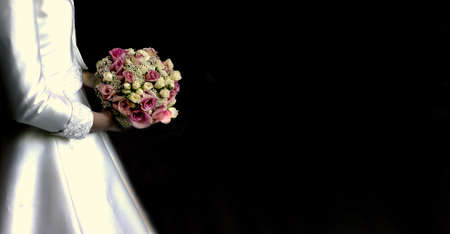 Bride is holding a beautiful bouquet arrangement against a long black backdropの写真素材