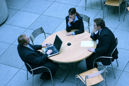 two men and woman are sitting around a table discussing business matters with a laptop on the table