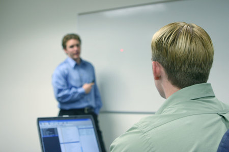 Two businessmen in green and blue shirts discuss business matters next to a marker board with a...