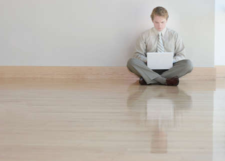 Businessman in tan shirt and tie is typing on his white laptop on wooden floorsの写真素材