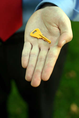 Businessman wearing blue shirt and red tie holds out his hand with a golden key in the middle of his palmの写真素材