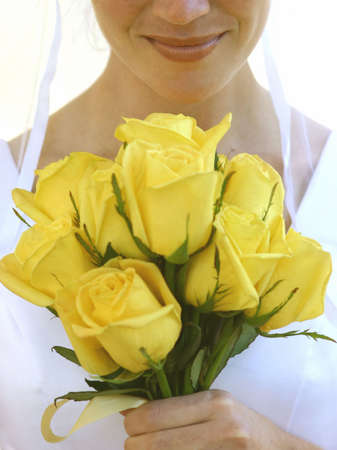 Beautiful bride smiles as she holds yellow roses in her handsの写真素材
