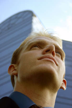 Blond hair blue eye business man wears blue shirt and blue tie looks off into the future in front of glass, blue office buildingの写真素材