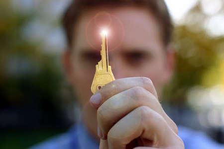 Business man holds up key to success with a light beaming on top of the keyの写真素材