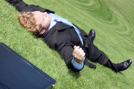 Business man has finally had it, collapses into relaxation on the green hill of tranquilityの写真素材