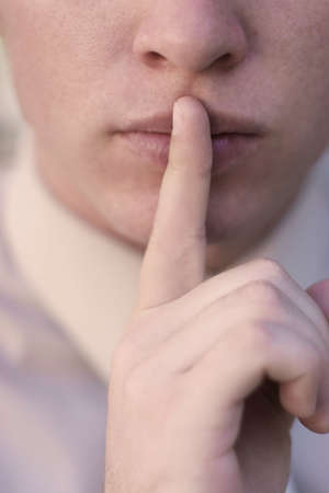 Businessman with tan shirt is placing index finger on his lips, an expression of being silentの写真素材