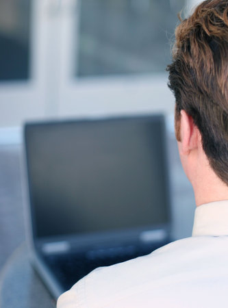 Businessman in tan shirt looks down at his laptop on, next to business office building
