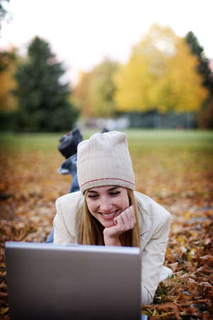 Woman with laptop relaxes in the fallen autumn leaves as she taps on her laptopの写真素材
