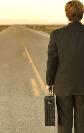 Businessman dressed in black suit is holding briefcase in the middle of the desert road, which leads to successの写真素材