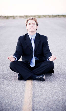 Younger businessman in black suit and blue tie sits in the middle of the road to successの写真素材