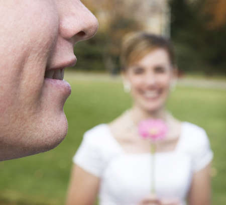 Woman is wearing a white wedding dress and holding a flower as man is smiling の写真素材