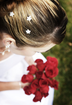 Woman dressed in wedding dress is holding roses on the green grass