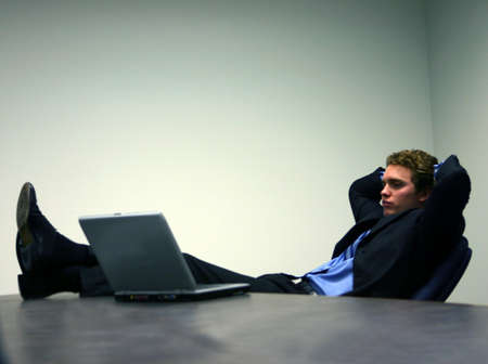 Business man in black suit and blue shirt is in relaxed position as he looks at his laptop screenの写真素材