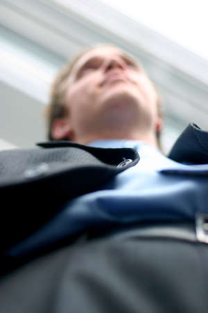 Business man in darker suit, blue shirt, and blue tie is posing in frornt of office building, shot from belowの写真素材