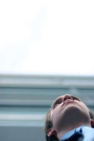 shot from below of the face of a business man in front of office buildingの写真素材