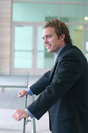 Business man in dark suit, blue shirt, and blue tie stands over glass with smile