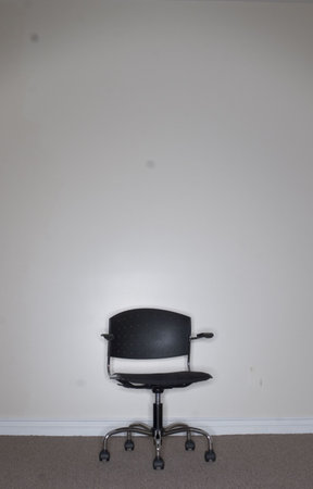 One Business Chair sits alone against a beige wall with nobody sitting in the chairの写真素材