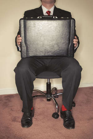 Businessman holding his own briefcase as defense while sitting in a business chair in a officeの写真素材