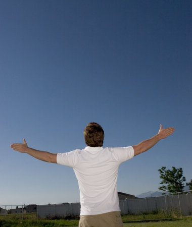 Young man raises his arms and looks up in the blue sky in his backyard