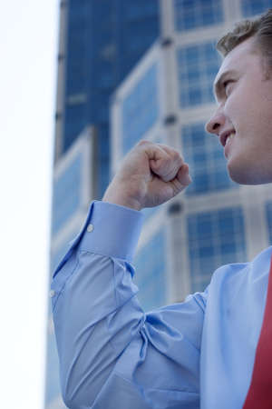 Businessman puts his hand in a fist in success while he wears a red tie and stands in front of a buildingの写真素材