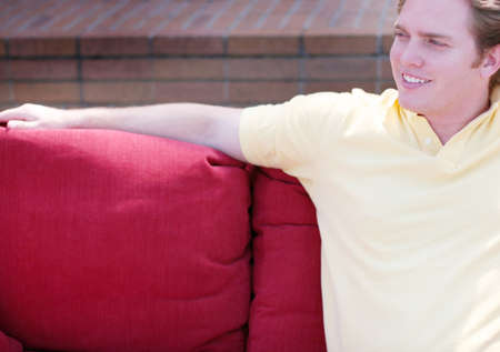 close-up of one young man sitting on red couch outside in front of brick wall の写真素材