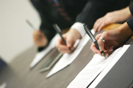 three hands holding pens signing document on tableの写真素材
