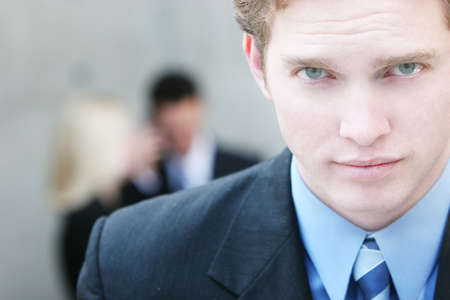 one businessman looking at camera with two people in background conversingの写真素材