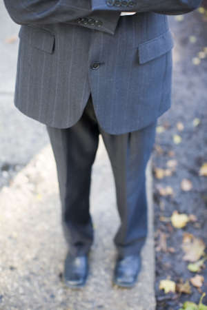 waist-down front shot of businessman folding arms wearing suit standing on sidewalkの写真素材