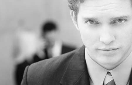 one businessman looking at camera with two people in background conversingの写真素材