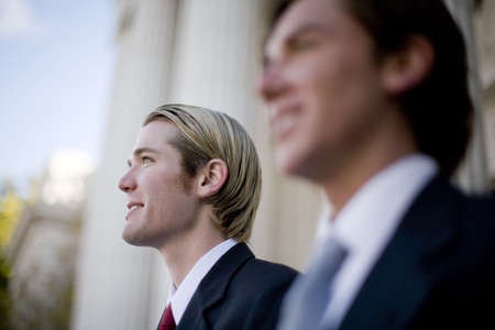 two businessmen standing side by side smiling in front of courthouseの写真素材