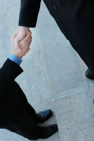 Businessmen giving a handshake to seal the deal. Each of the businessmen are wearing black suits and standing tallの写真素材