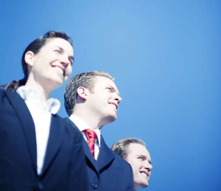 Three business people standing smiling looking away in same direction wearing full suitsの写真素材