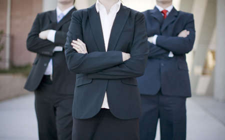 three business people standing wearing full suits with arms crossedの写真素材