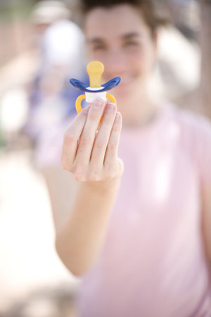 woman holding a pacifier up to the camera with her hand while wearing a pink shirt and smiling...