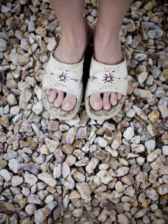 view of womans feet wearing sandals on pile of rocksの写真素材