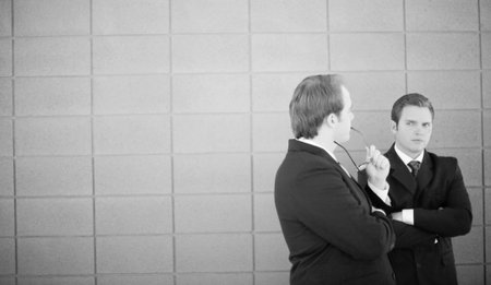 two businessmen in suits standing and talking with each other with brick backgroundの写真素材
