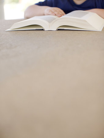a young child is reading a book on the table with a lot of space at the bottom of the image