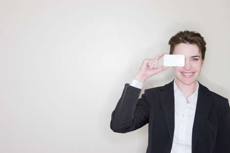 Businesswoman showing her business card and covering one eye with her business cardの写真素材