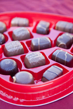 A box of valentine's day chocolates is open with many pieces of chocolates in open view in a red heart shaped boxの写真素材