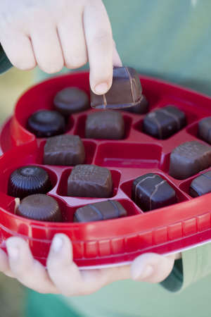 A young child is grabbing a piece of chocolate out of a box of valentine's day chocolate with his fingers and holding one piece of chocolate の写真素材