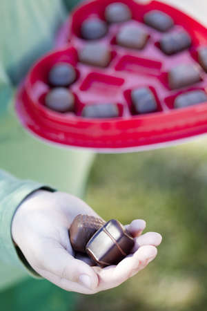 A young child is handing out two pieces of valentine chocolate from a heart shaped box while giving the chocolate in his handsの写真素材