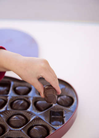 a girl is grabbing a piece of chocolate from a box of heart shaped chocolates の写真素材