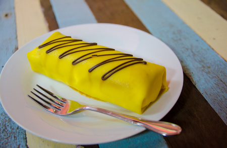 banana crape cake on white plate on wooden table, focus on center of pieceの写真素材