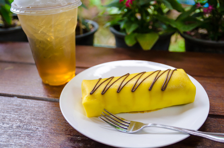 banana crape cake on white plate with lemon tea, focus on cake near forkの写真素材
