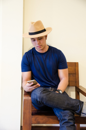 asian wear blue T-shirt siiting on wooden chair holding smartphoneの写真素材
