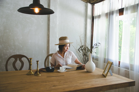asian women sitting and reading book, looking to windowの写真素材