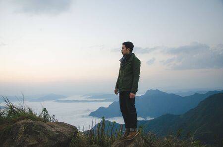 young man standing on hill is wearing green coatの写真素材