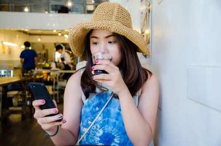 asian girl is holding phone and drinking in coffee cafeの写真素材